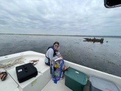 Woman sits on a boat with a clipboard, recording data