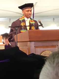 Kai Hardy stands behind a podium wearing a cap and gown and gives a speech during a Vermont Law School graduation ceremony