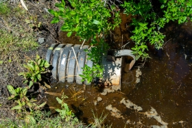 A floodgate and pipe sit in murky ditch water.