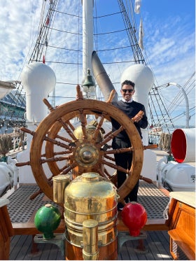 Abdulmajid Alrefaie stands behind the large wooden wheel of a ship