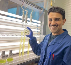 Man in lab coat holds up a petri dish with cultures visible on it