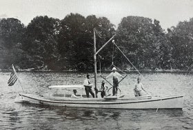 Four men stand on a small boat equipped for examining oyster grounds, as one man sits inside and pilots the boat