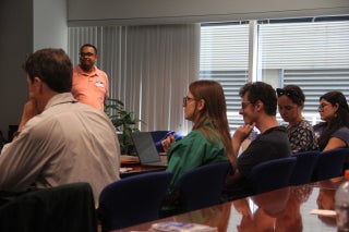 A group of researchers seated at a table listen to a presentation