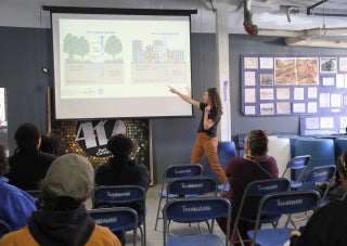 A woman shares a presentation on harvesting stormwater with a small group of people seated in chairs