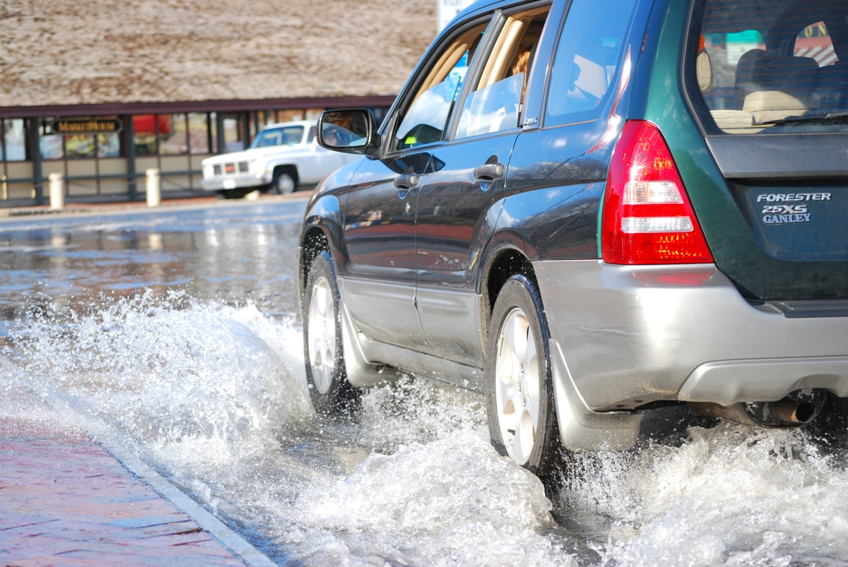 A sports utility vehicle drives through a street flooded with water.