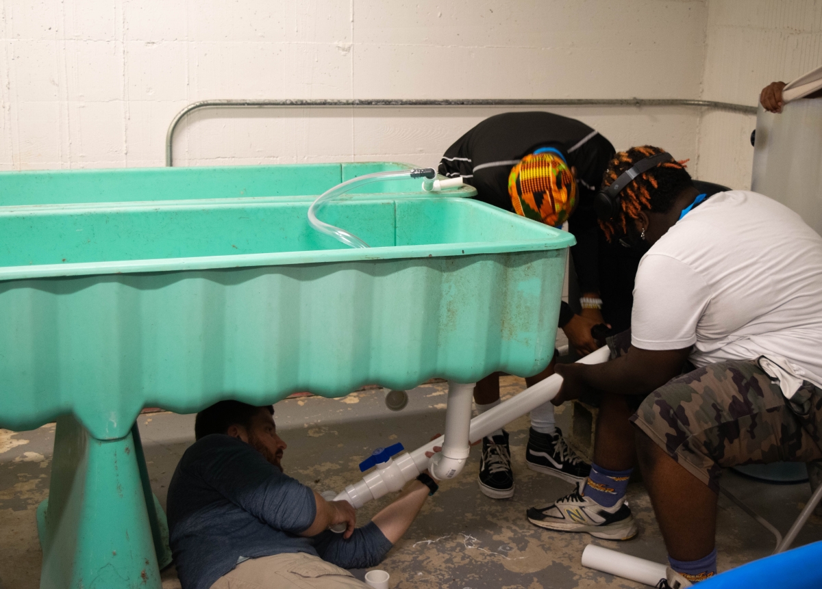 Two students at Green Street Academy assist MDSG Aquaculture Education Coordinator Chris Flight to assemble portions of an aquaculture system. Photo: Manal Murangi, MDSG