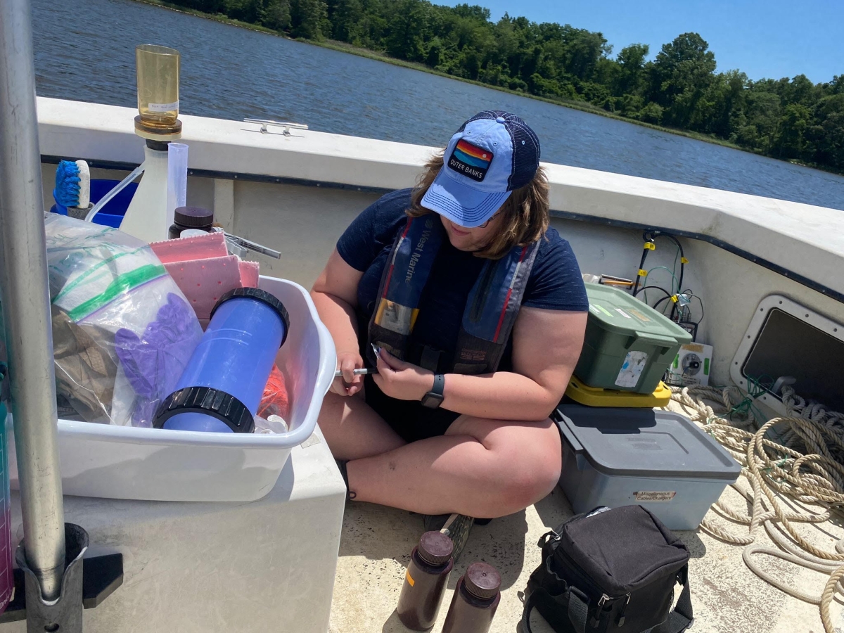A young woman sitting on a boat deck surrounded by bins of research equipment and ropes