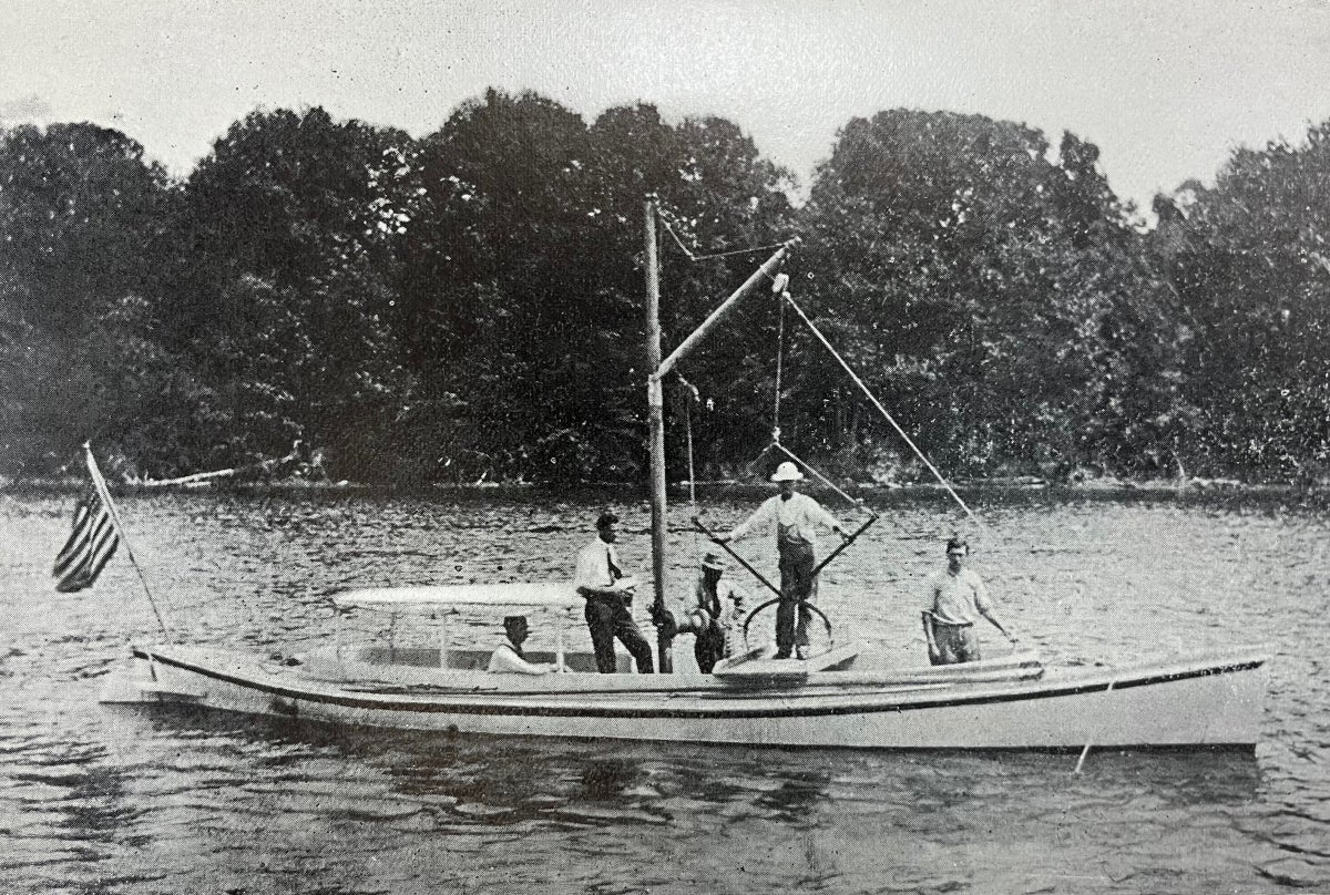 Four men stand on a small boat equipped for examining oyster grounds, as one man sits inside and pilots the boat