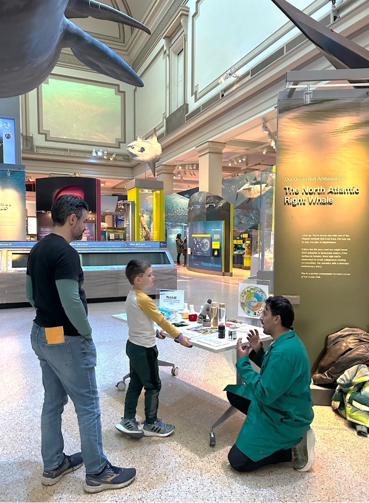 A man in a lab coat kneels next to a display table in the Sant Ocean Hall as he speaks with a young boy