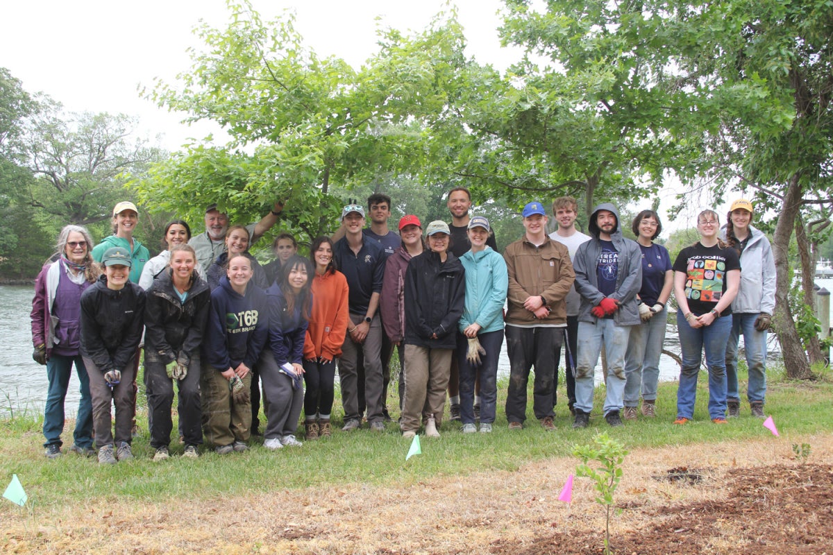 A group of volunteers wearing gardening gloves and rain gear stand together along the shoreline at the Wye Research and Education Center next to a newly planted garden 