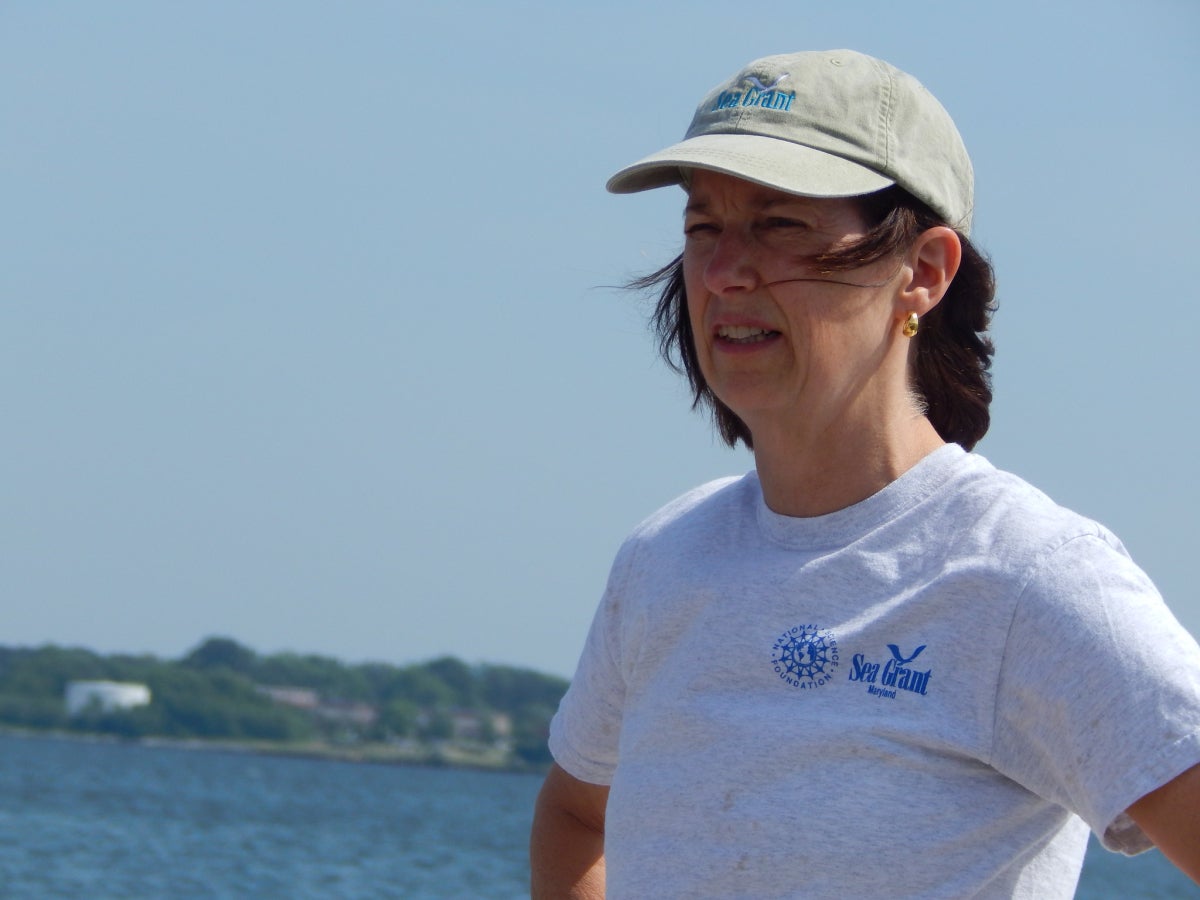 Fredrika Moser in a baseball cap and Sea Grant T-shirt stands near a body of water